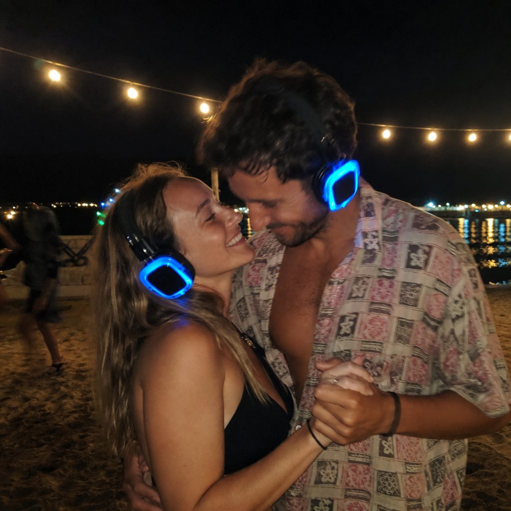 Couple dancing on the beach in blue LED headphones